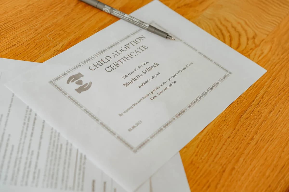 Close-up of a child adoption certificate and documents with a pen on a wooden table.