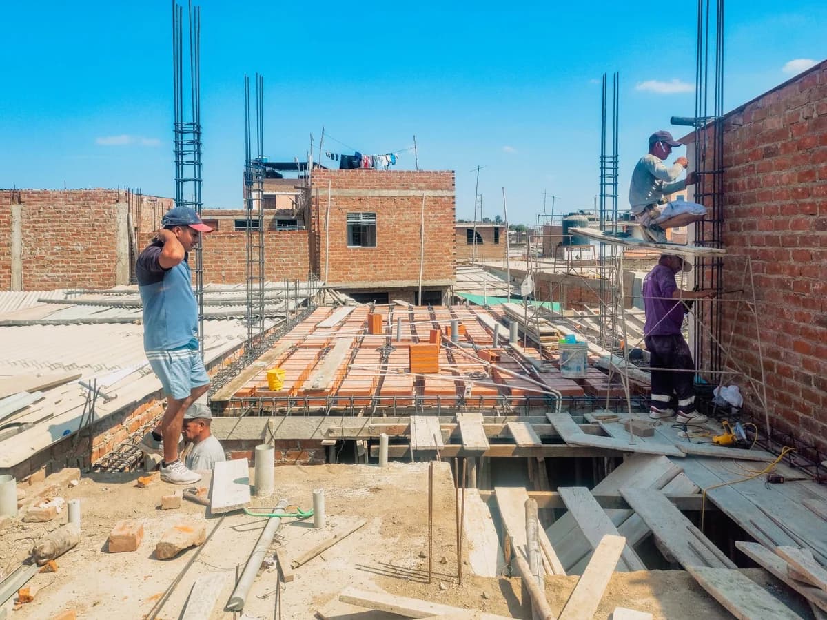 Construction workers building a structure in Lambayeque, Peru, under a clear blue sky.