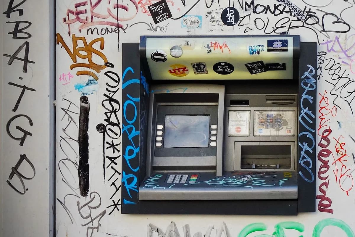 An ATM embedded in a graffiti-covered wall, showcasing vibrant street art in a city setting.