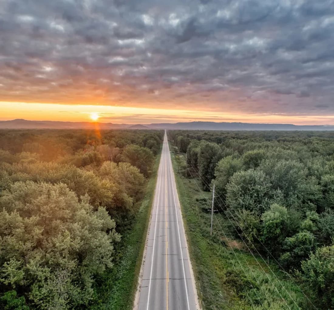Road stretching toward a sunset horizon through forest