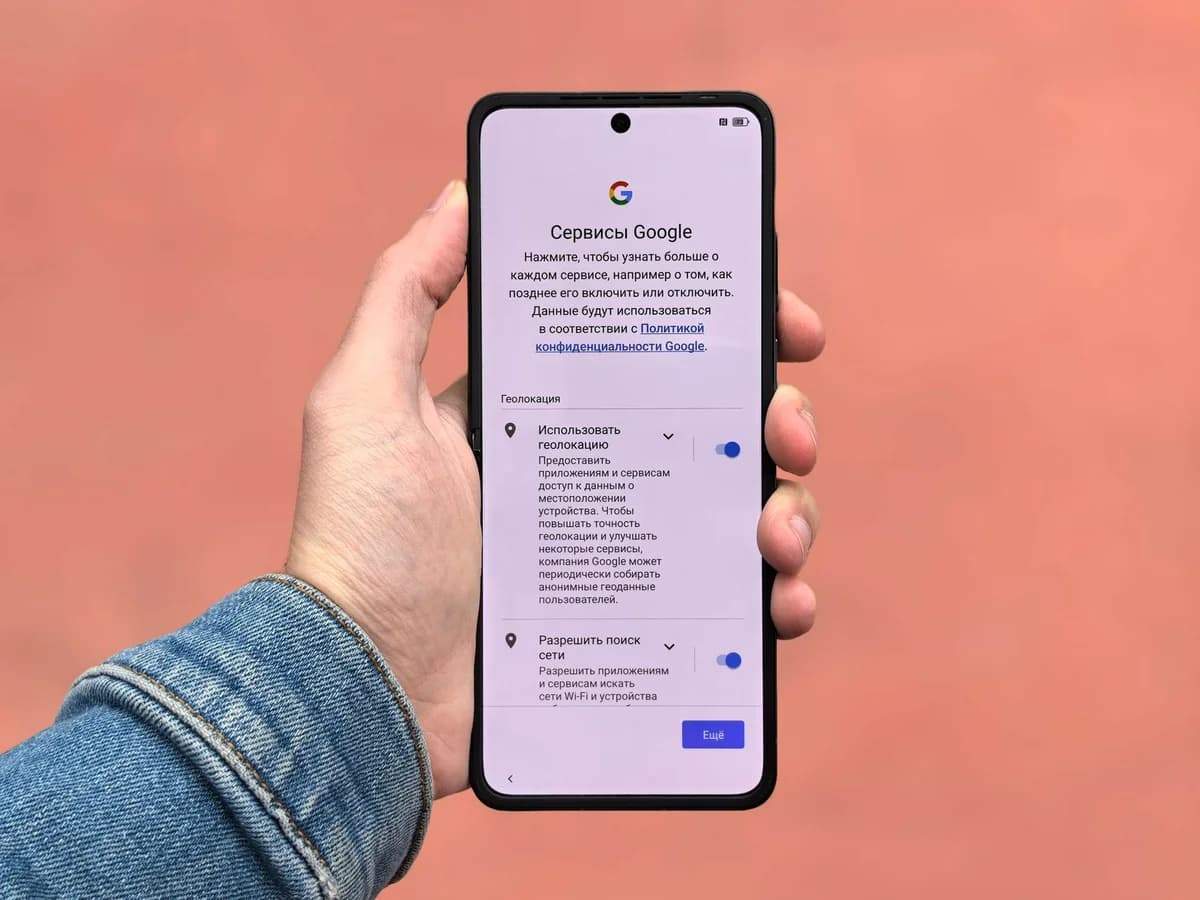 A person holding a smartphone displaying Google settings on a simple background.
