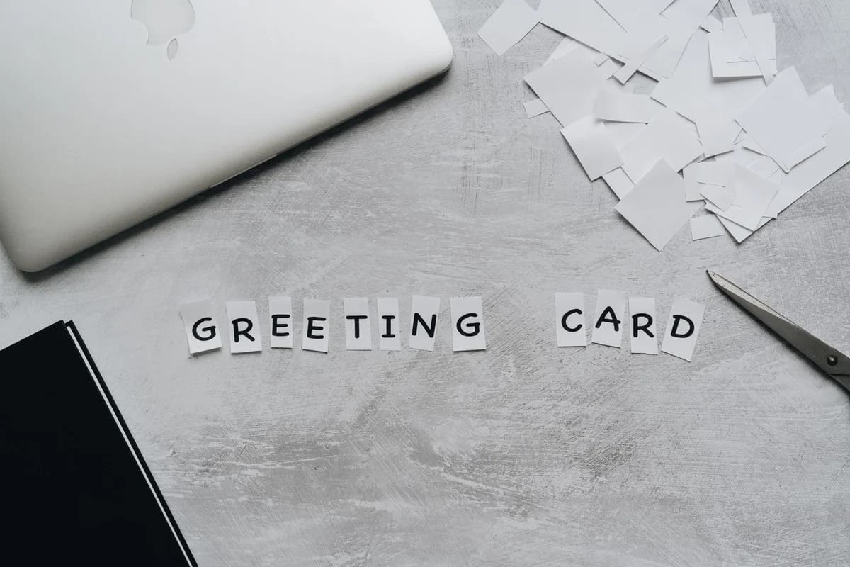 Top view of greeting card arrangement with paper, scissors, and laptop on a gray surface.
