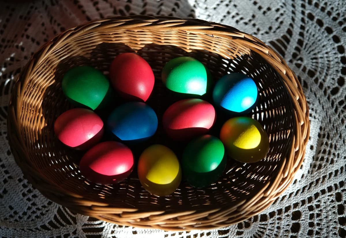 Brightly colored Easter eggs in a wicker basket on a crocheted tablecloth, in sunlight.