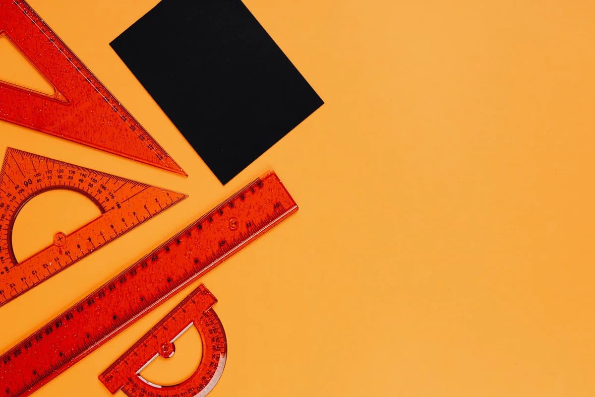 Top view of colorful geometric rulers and tools on a vibrant orange background.