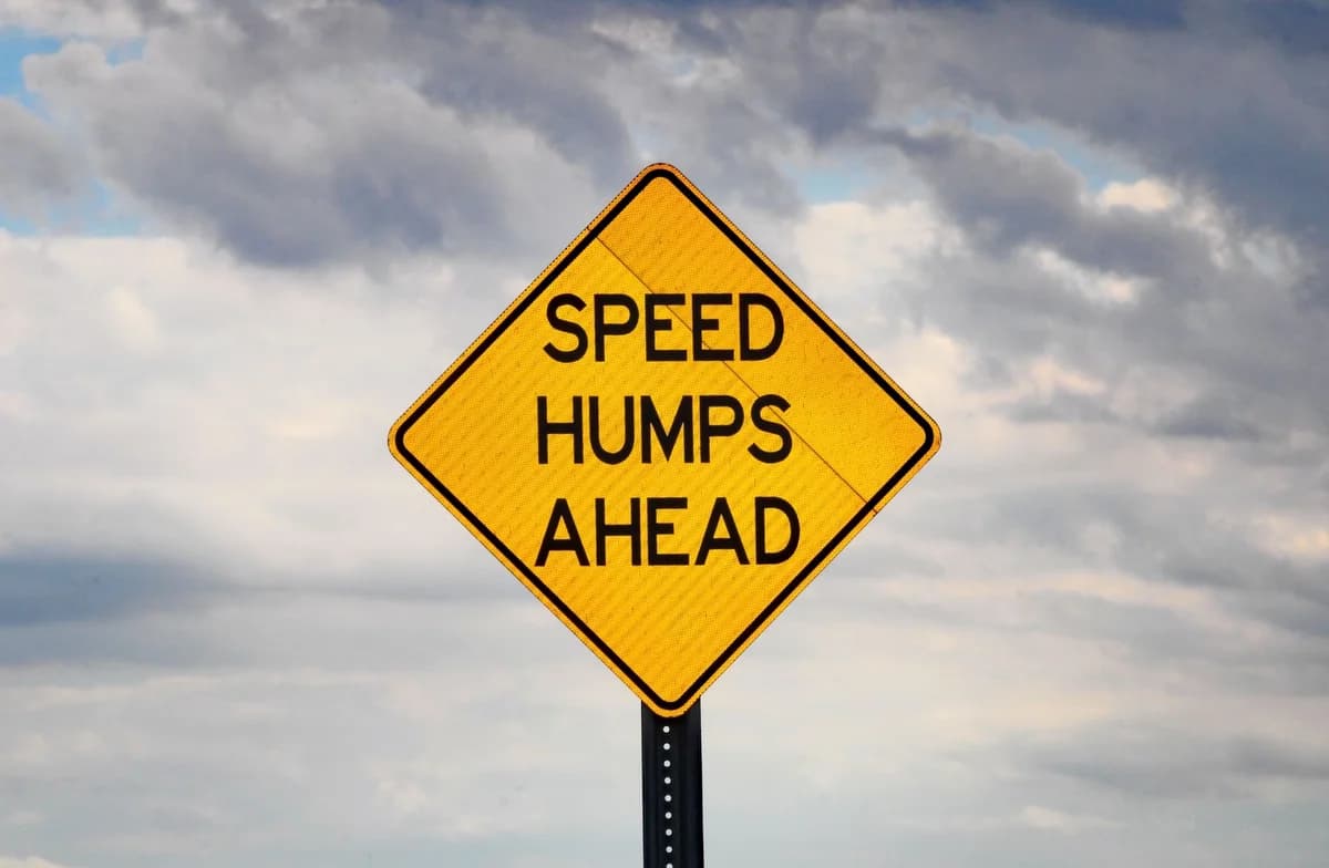 A speed hump warning sign under a cloudy sky, emphasizing safety.