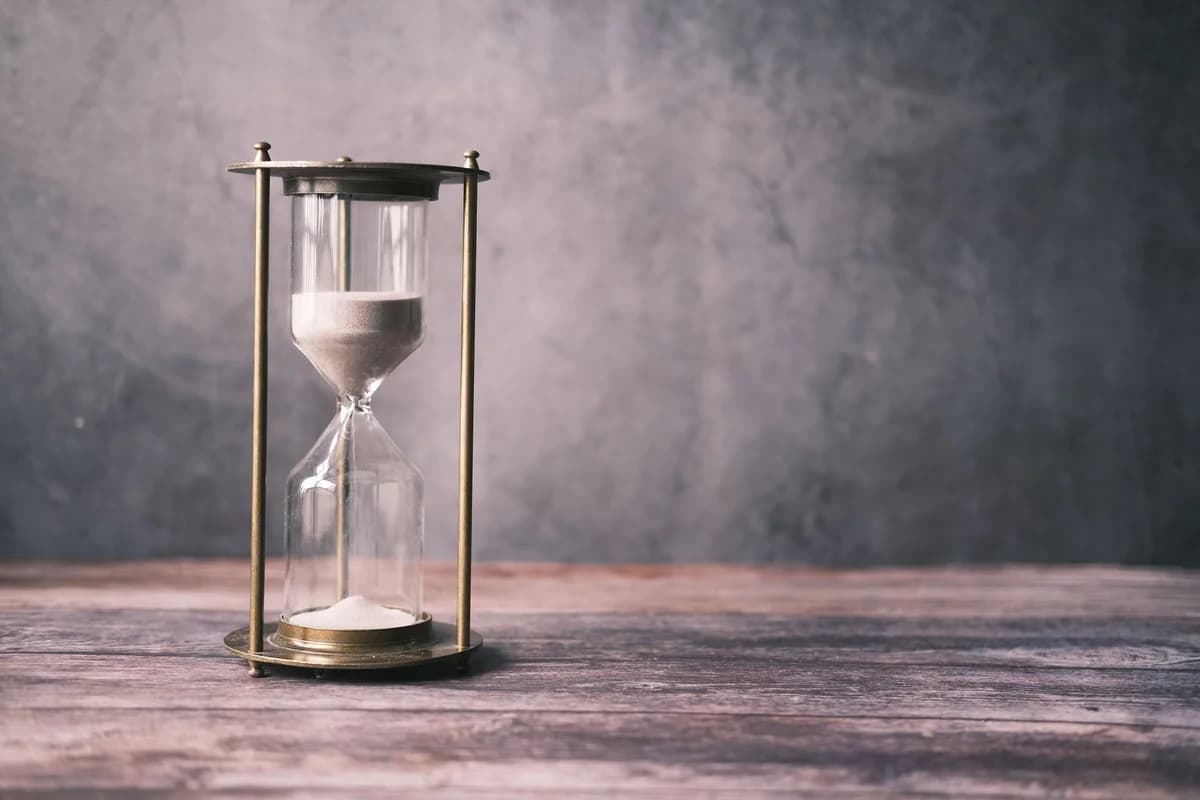 A classic hourglass with sand on a rustic wooden table against a soft gray background, offering ample copy space.