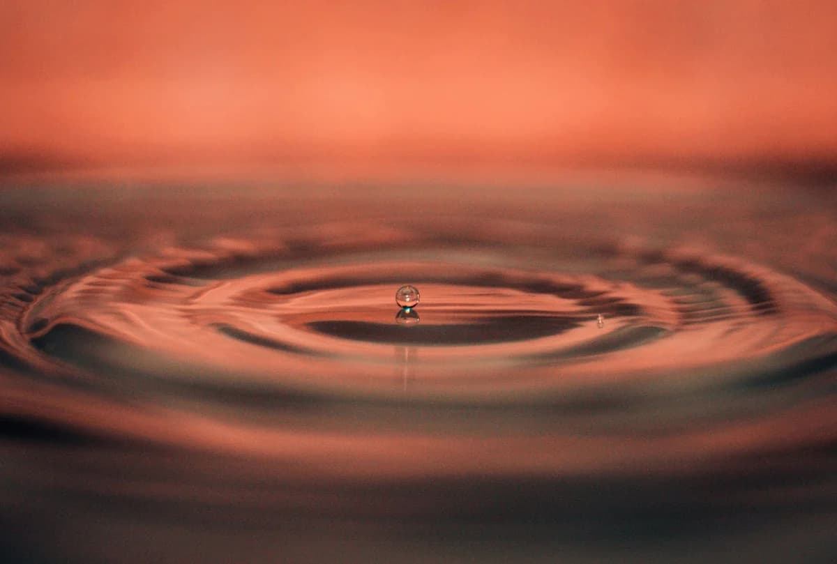 A captivating macro photograph capturing a single water droplet creating ripples on a calm water surface.