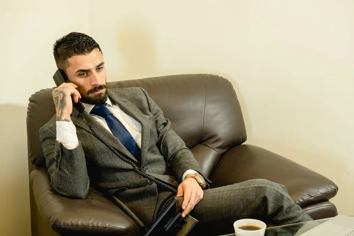 Bearded man in gray suit talking on the phone while seated in a modern office.