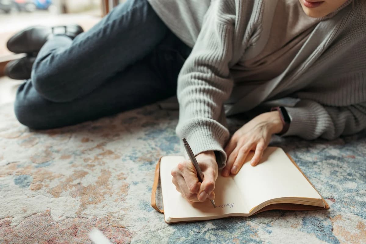 A person lies comfortably on the floor, writing in a journal with a pen, symbolizing creativity and relaxation.