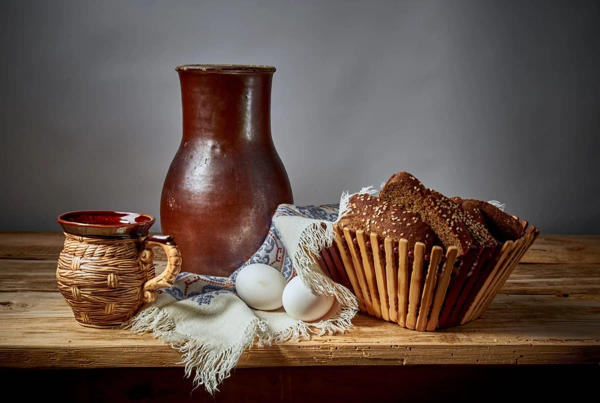 A rustic still life featuring bread, eggs, and pottery on a wooden table in a classic setting.