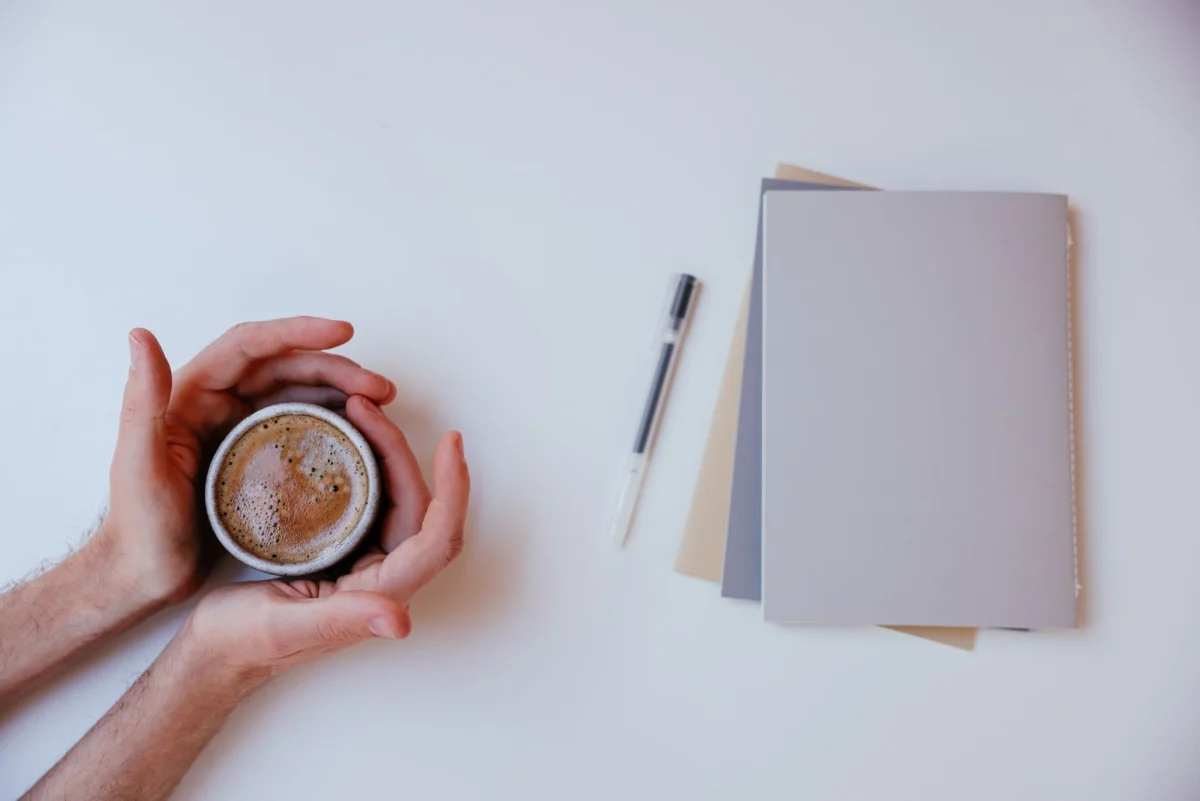 Hands holding a coffee cup at a calm morning desk