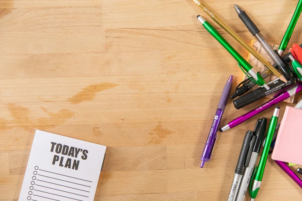 Flat lay of colorful pens, markers, and a notepad on a wooden surface with copy space.