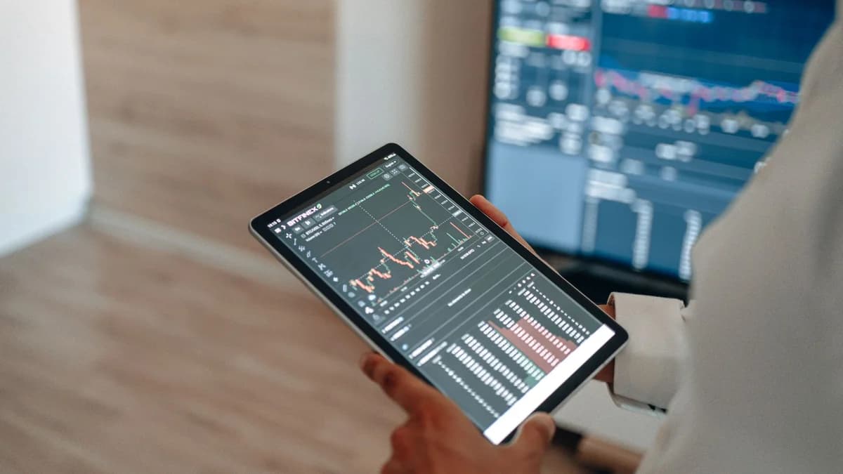 A person uses a tablet to monitor stock market trends and real-time trading graphs.