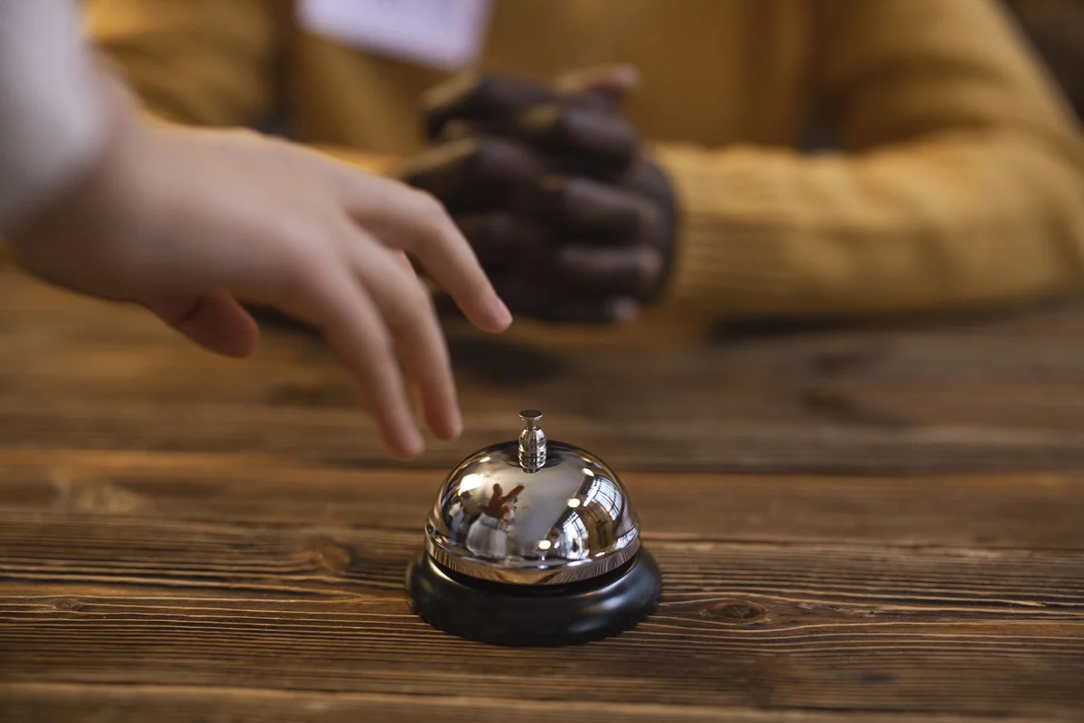 A hand reaching for a reception bell on a wooden table, indicating service or hospitality request.