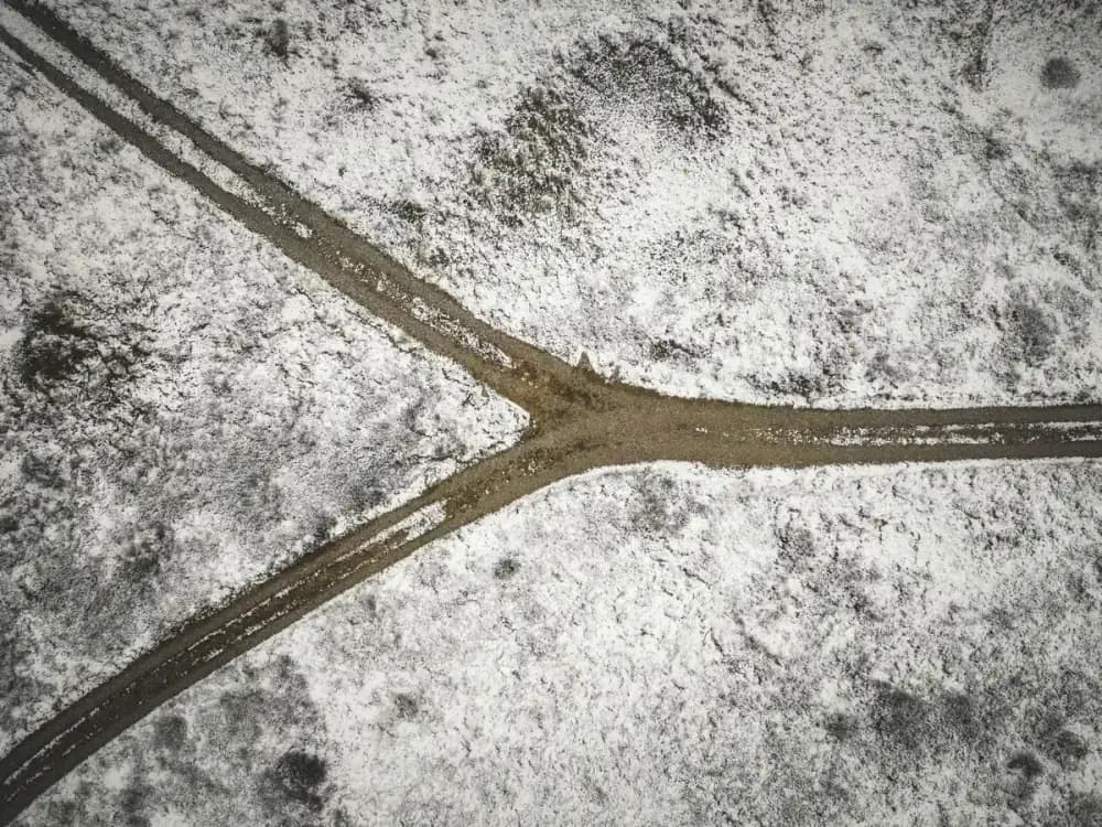 Drone shot of a snowy landscape with a forked dirt road in Bindslev, Denmark.
