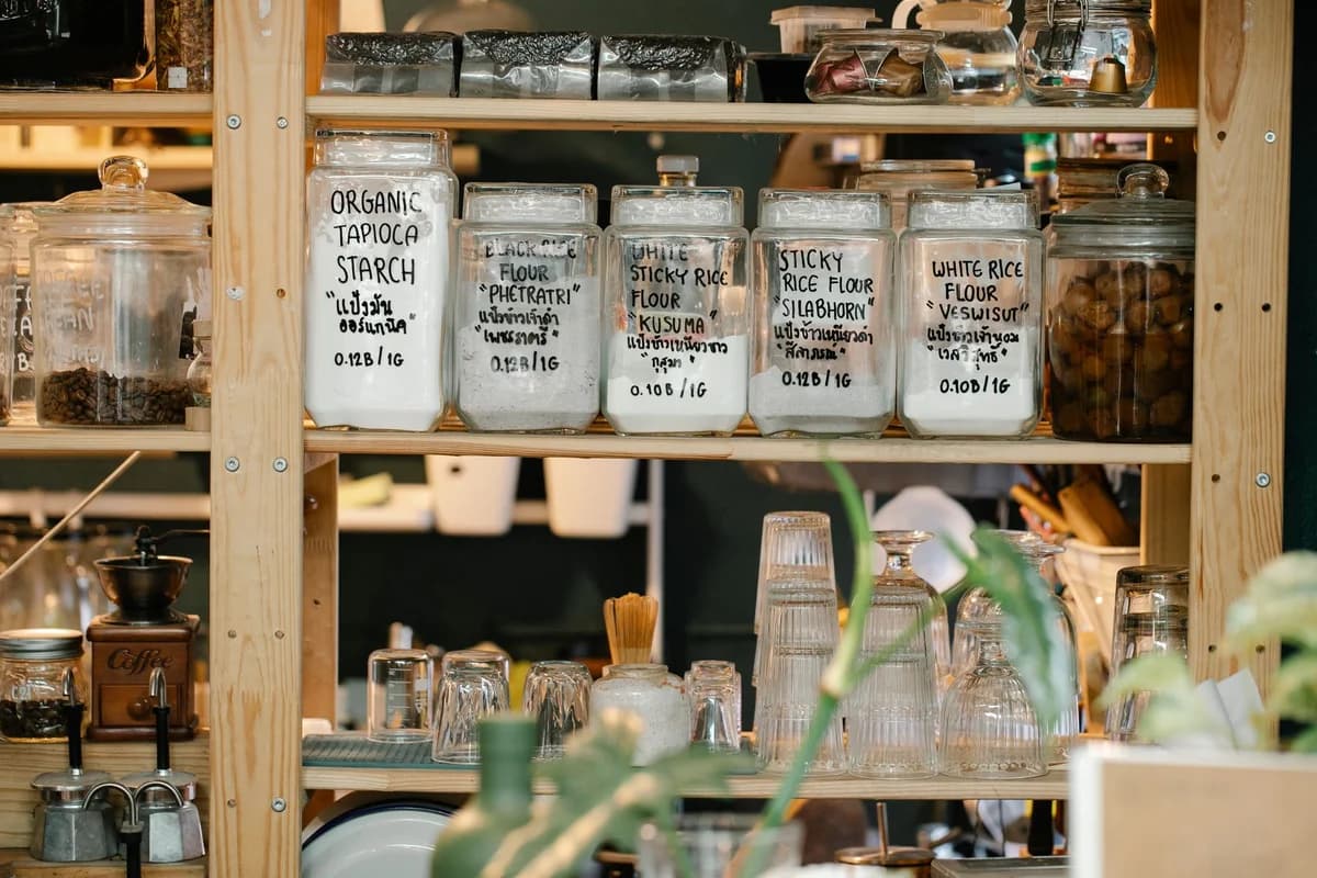 Collection of various glass jars with different dry food and glassware placed on wooden shelf