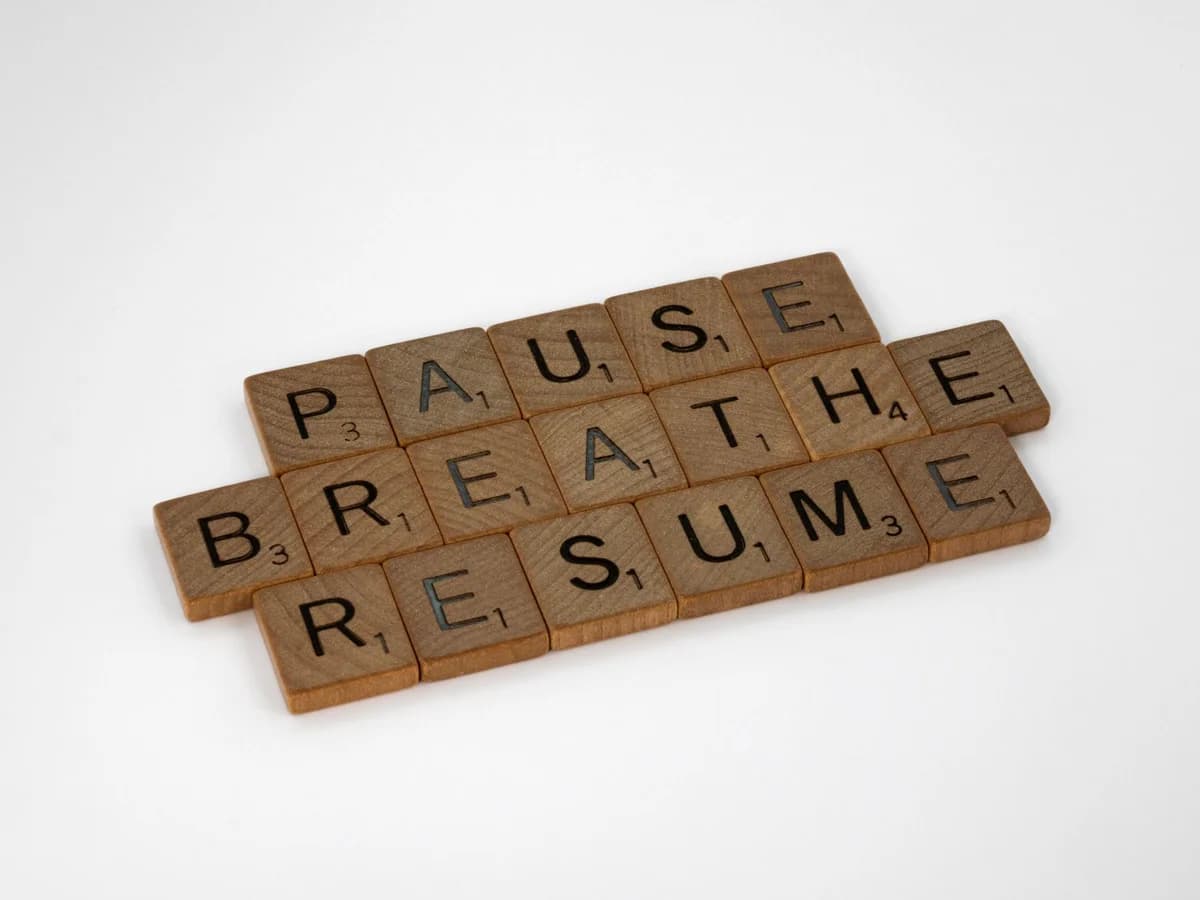 Inspiring words 'Pause Breathe Resume' arranged with scrabble tiles on a white surface.