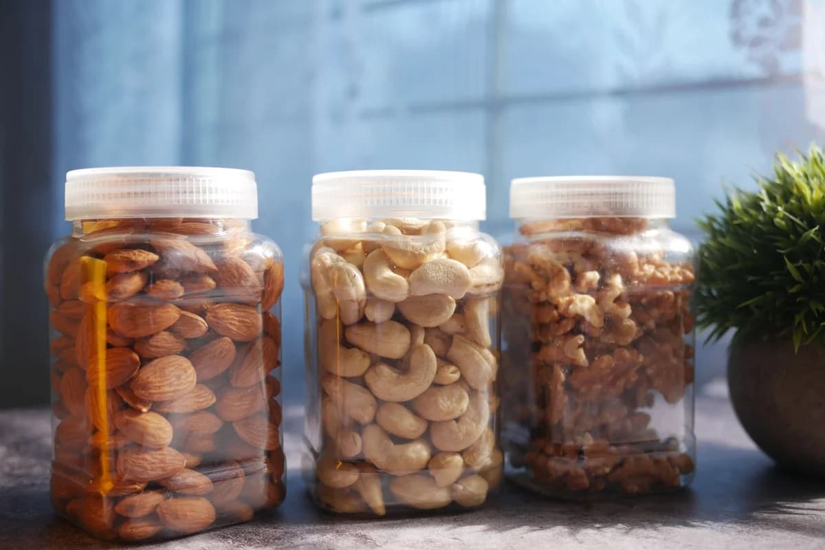 Vibrant display of almonds, cashews, and walnuts in plastic jars on a kitchen countertop.