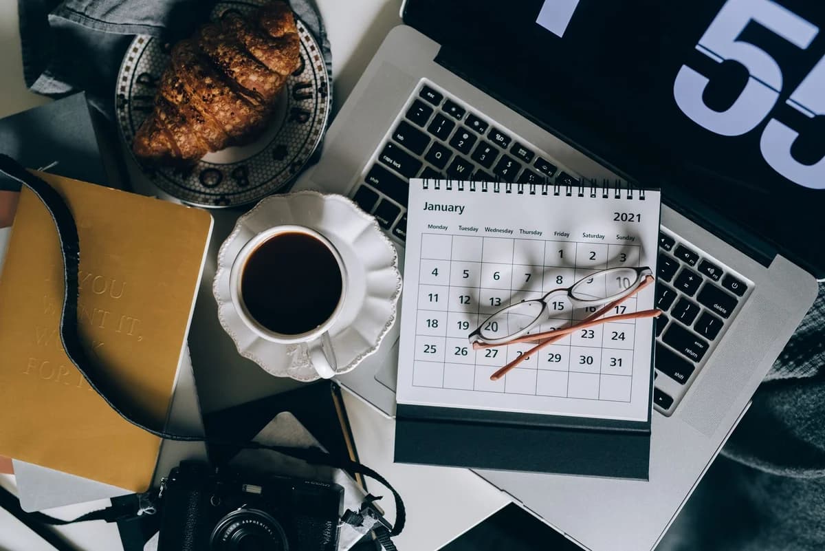 A serene workspace setup with coffee, croissant, laptop, and calendar, ideal for organizing plans.