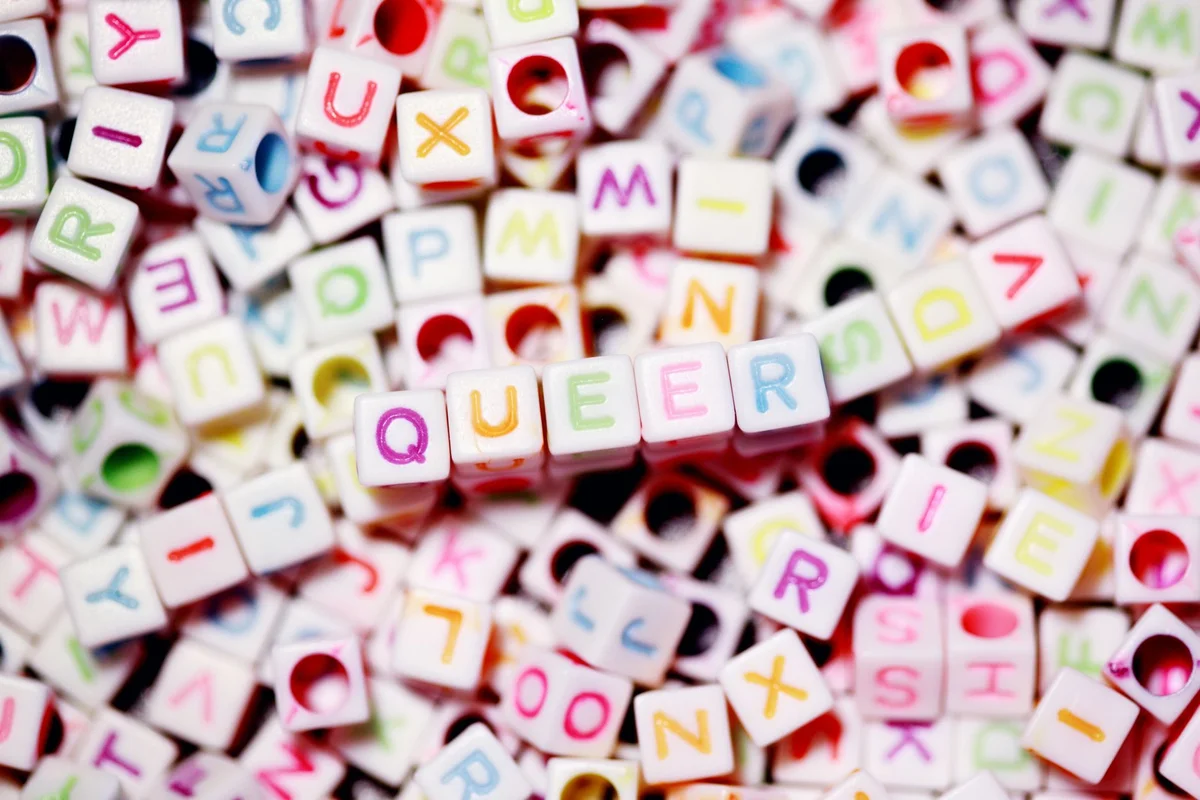 Close-up of colorful alphabet beads spelling out 'QUEER' on a blurred background.
