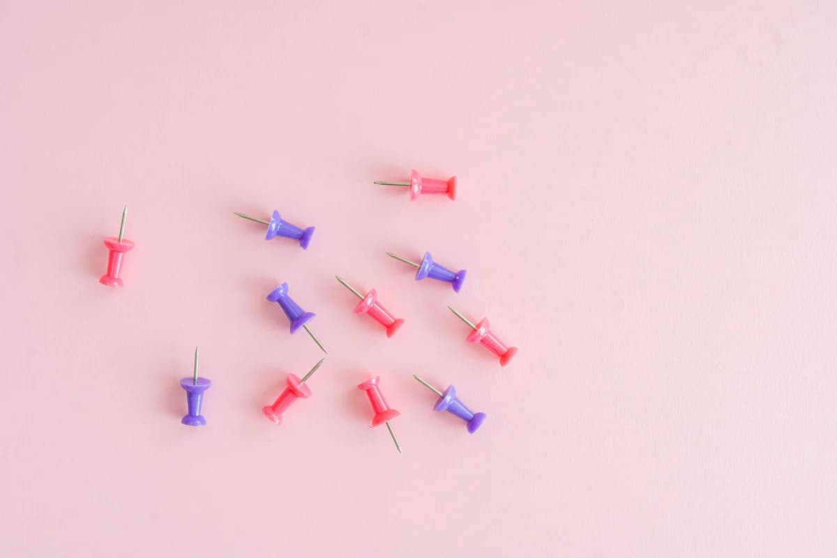 Vibrant red and purple thumbtacks scattered artfully on a pastel pink background.