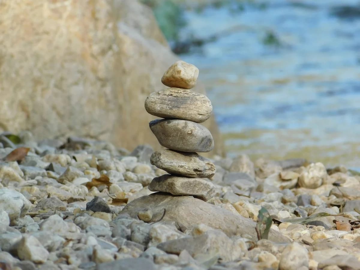 Serene image of a balanced stack of pebbles by a flowing river, evoking peace and tranquility.