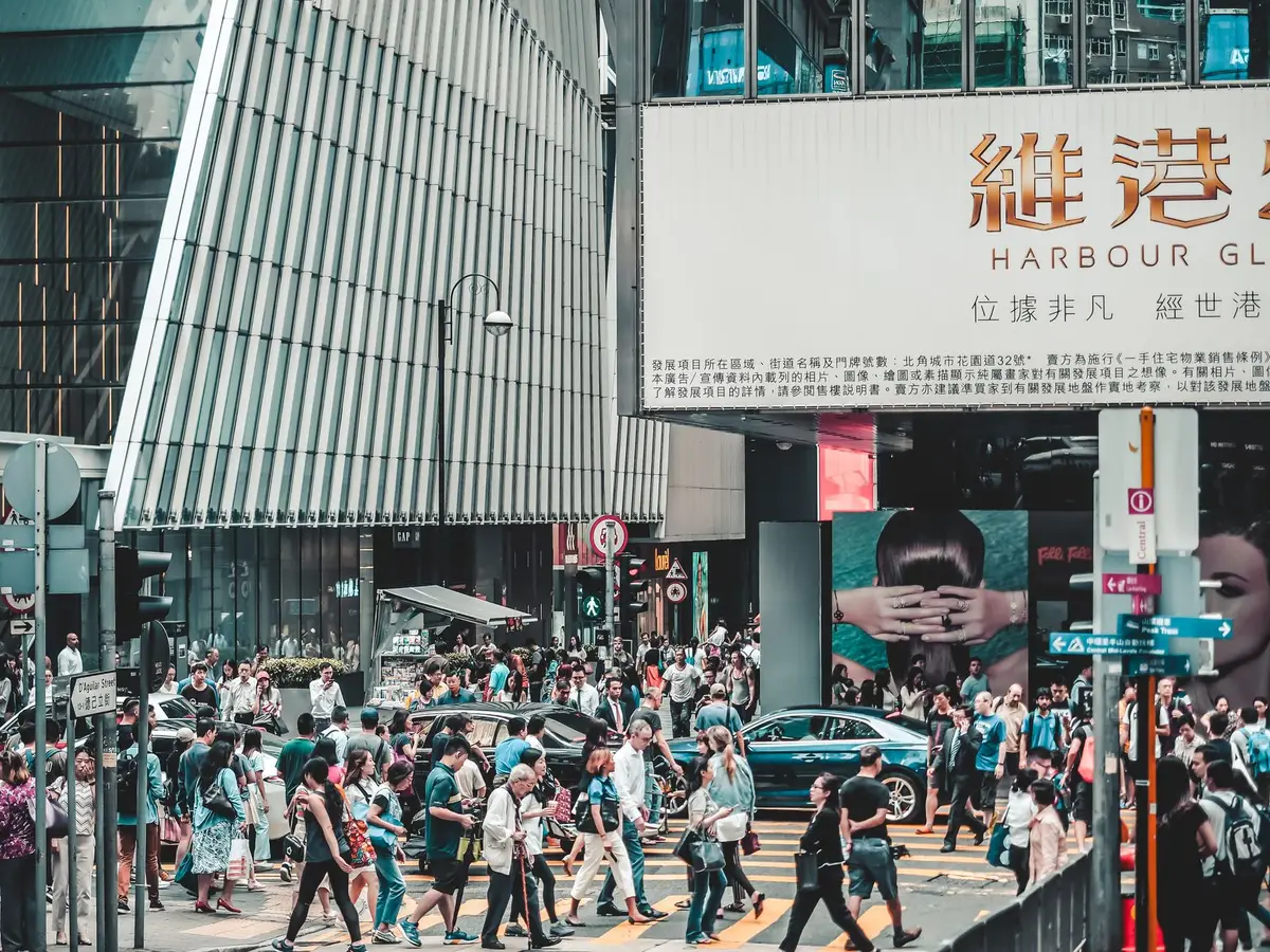 Crowd of people crossing street in busy Hong Kong shopping district under large signs.